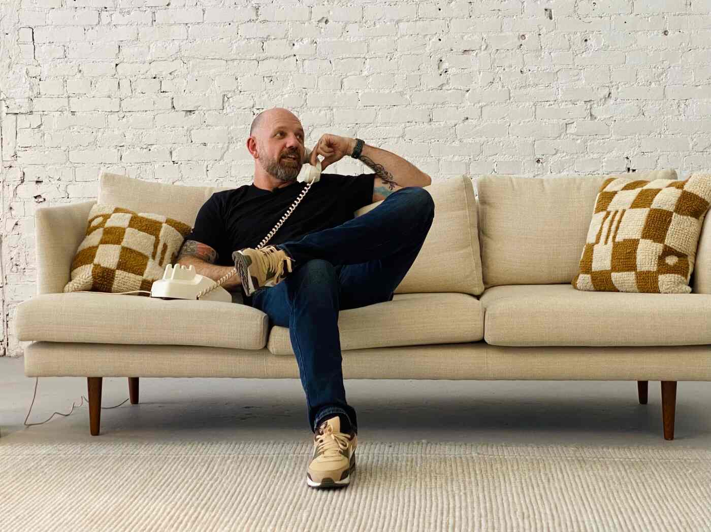 Huck Gee seated on a sofa, speaking on a corded telephone.