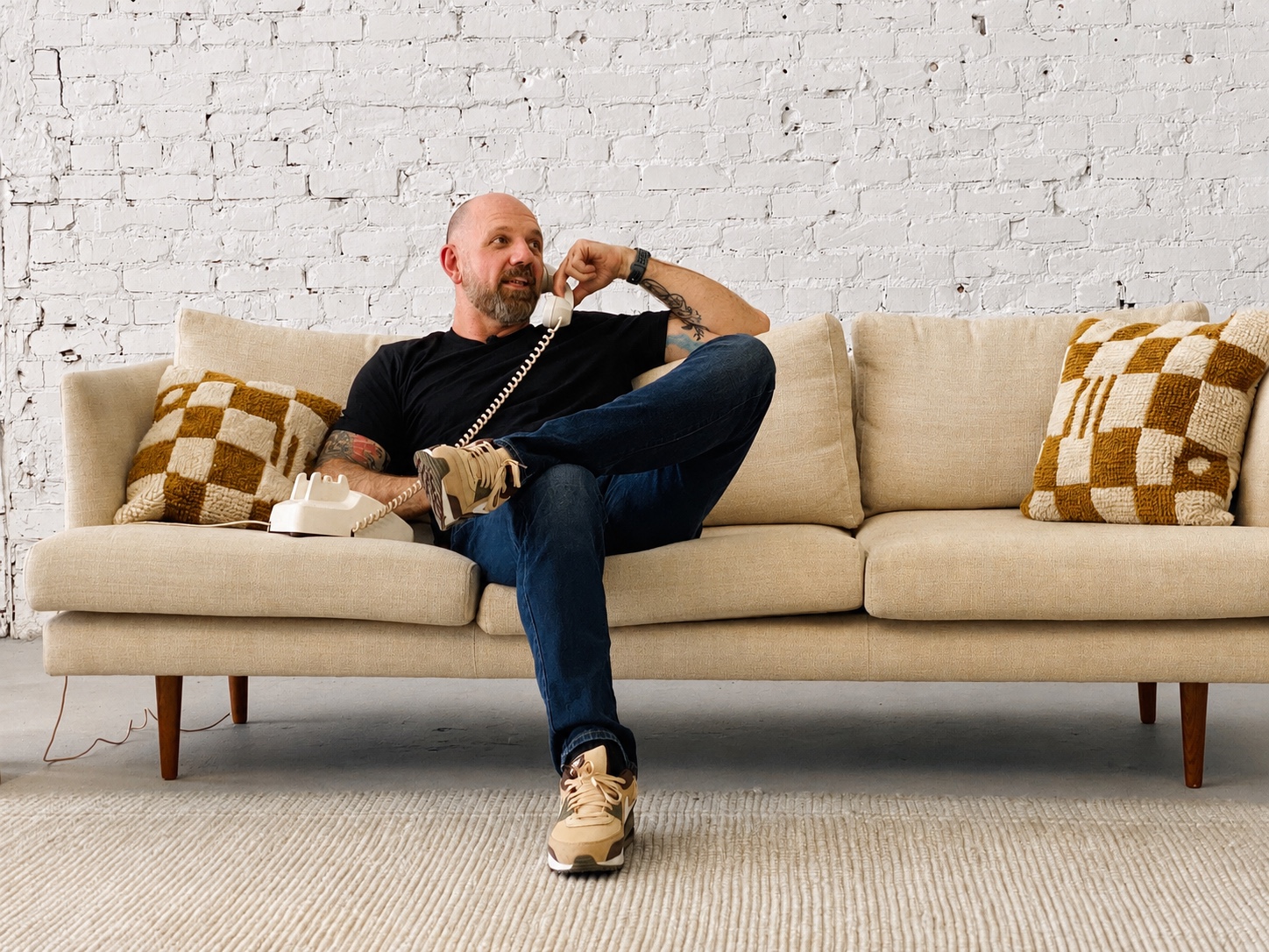 Huck Gee seated on a sofa, speaking on a corded telephone.